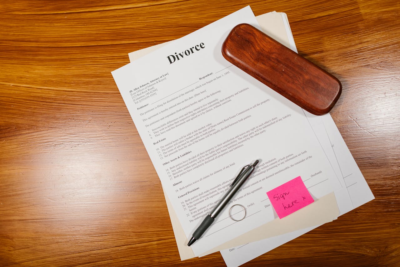 Flat lay of divorce papers with a pen and ring on a wooden table for legal themes.